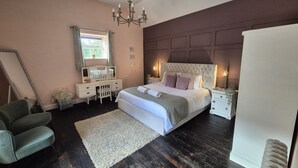 A bedroom with a large bed, a dresser, a vanity with a mirror, a chair, and a chandelier. - Squirrel Cottage (Ballymena)