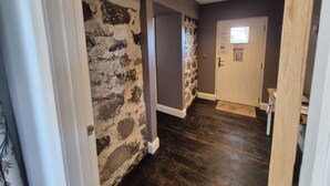 A hallway with a stone wall, wooden flooring, and a door with a window. - Squirrel Cottage (Ballymena)