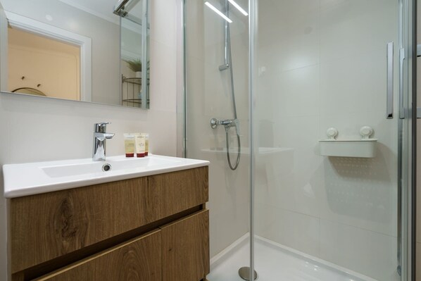A modern bathroom with a white sink, wooden cabinets, a glass shower enclosure, and a mirror above the sink.