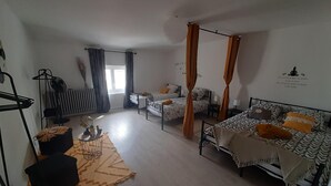 Ein Schlafzimmer mit zwei Betten, einem Standventilator, einem Heizkörper und einem Fenster mit Vorhängen.