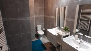Ein modernes Badezimmer mit zwei Waschbecken, einer Toilette, einer Dusche und einem Spiegel.