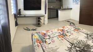 Una sala moderna con televisor de pantalla plana, un sofá con funda floral, una cocina al fondo y un comedor.