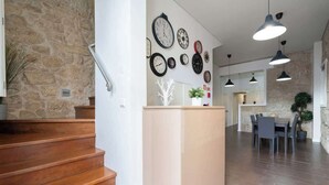 A modern interior with a stone wall, wooden staircase, a central island with a plant, and a dining area with pendant lighting. - Cozy House w Balcony by HostWise (Porto)