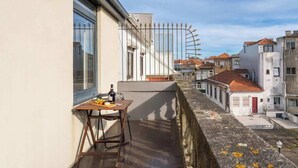 A balcony with a table, a bottle, and a glass, overlooking a street with buildings. - Cozy House w Balcony by HostWise (Porto)