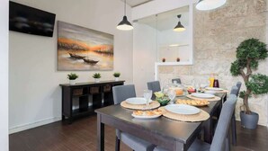 A dining area with a long table set for a meal, a painting on the wall, and a stone wall with a plant. - Cozy House w Balcony by HostWise (Porto)