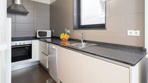 A modern kitchen with white cabinets, a stainless steel range hood, a microwave, and a window above the sink. - Cozy House w Balcony by HostWise (Porto)