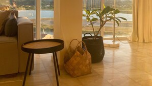 A spacious room with a large window offering a view of a body of water and distant hills. There is a sofa, a small round table, and a potted plant. - Best View-Stylish Penthouse with communal pool (Kerkira)