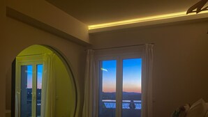 A bedroom with a large bed, a view of the sunset through the window, and a circular mirror on the wall. - Best View-Stylish Penthouse with communal pool (Kerkira)