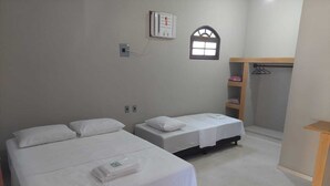 Una habitación con dos camas individuales, una ventana pequeña, un perchero y un estante de madera.