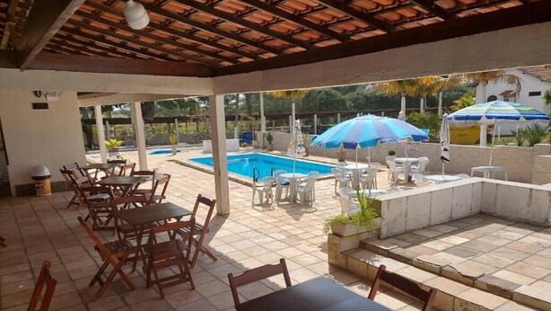 Un espacio al aire libre cubierto con mesas y sillas de madera, una piscina y sombrillas.
