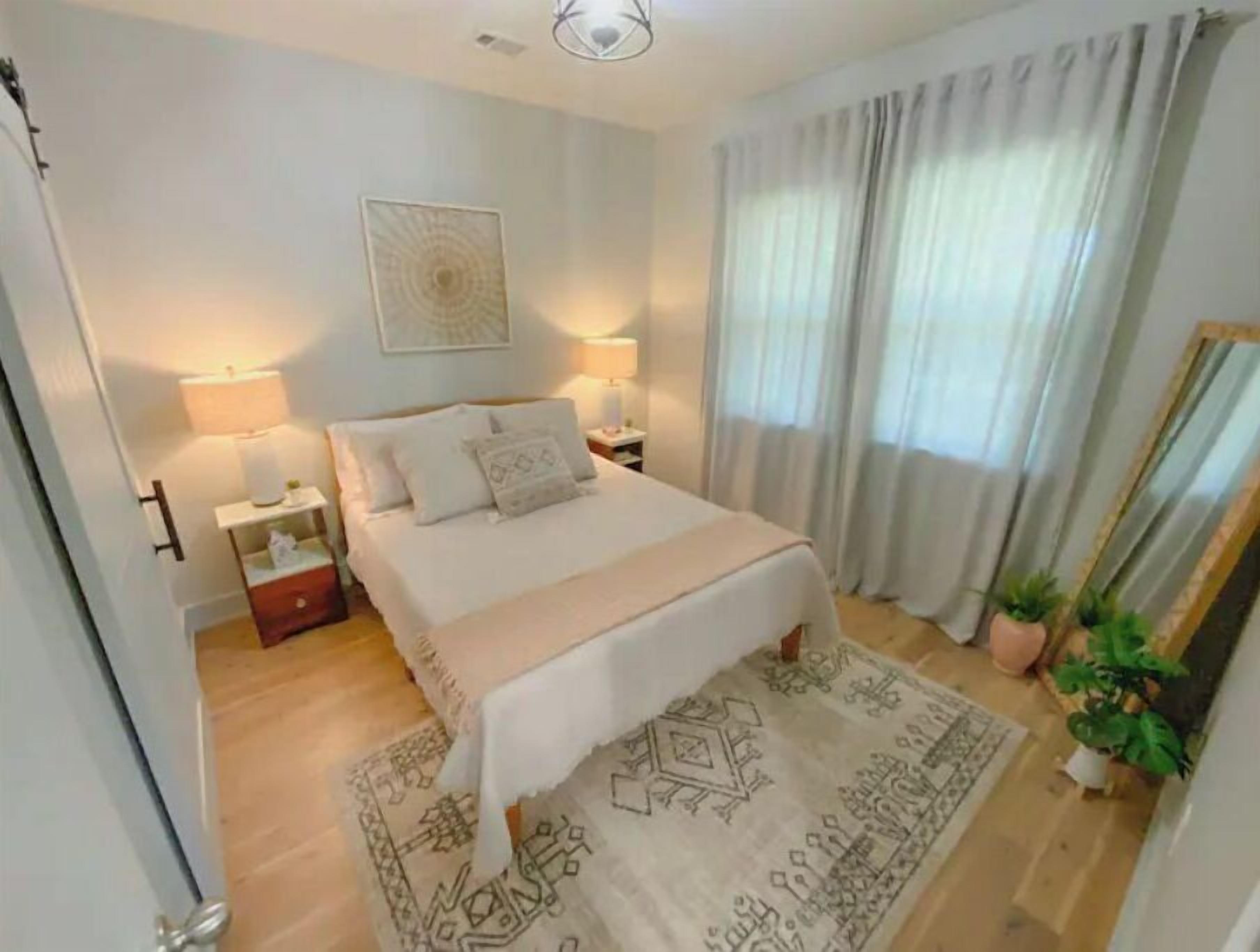A bedroom with a bed, nightstands, a mirror, and a patterned rug.