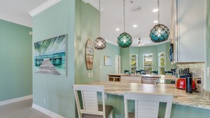 Cocina con isla central, luces colgantes y decoración con una tabla de surf.