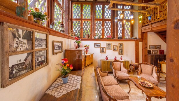 A cozy, rustic room with wooden furniture, a wooden ceiling, and large windows with lattice designs. - Serbetci Garden Konak (Safranbolu)