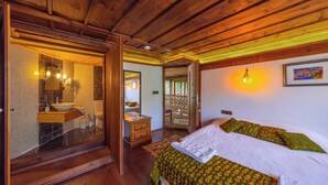 A wooden ceiling, a bed with green patterned bedding, a bathroom with a sink and mirror, and a door leading outside. - Serbetci Garden Konak (Safranbolu)