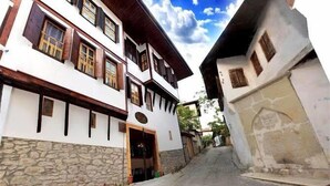 A traditional two-story building with a stone base and wooden upper structure, featuring a central entrance and multiple windows with shutters. - Serbetci Garden Konak (Safranbolu)