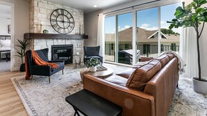 A modern living room with a stone fireplace, leather sofa, and a large sliding glass door leading to a balcony.