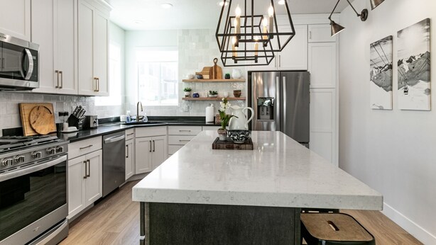 A modern kitchen with white cabinets, stainless steel appliances, a central island, and a hanging light fixture.