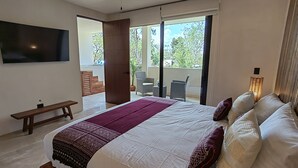 A bedroom with a large bed, a bench, a TV, and a balcony with outdoor furniture. - ITZÁ ALDEA ZAMÁ - BOHO CHIC con Alberca (Tulum)