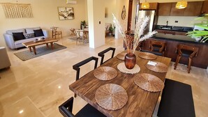 A modern kitchen with a central island, a dining area with a wooden table and woven placemats, and a living room with a sofa and coffee table. - ITZÁ ALDEA ZAMÁ - BOHO CHIC con Alberca (Tulum)