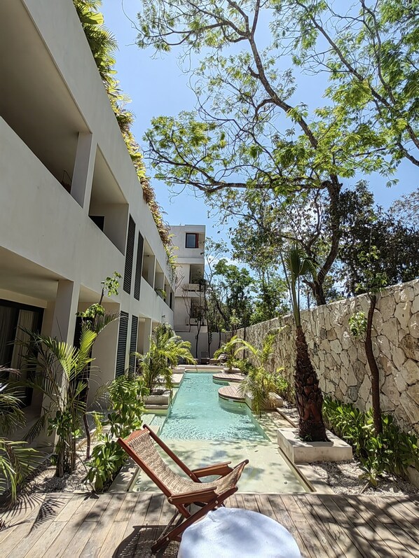 A pool area with lounge chairs, a stone wall, and a building with balconies.