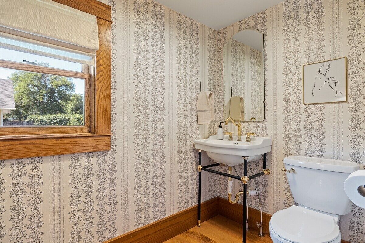 Un baño con ventana, lavamanos, inodoro y espejo.