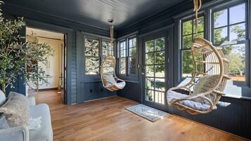 A room with a large window, a hanging chair, a wooden floor, and a sofa.