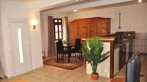 A living room with a wooden dining table, chairs, a TV, and a potted plant.