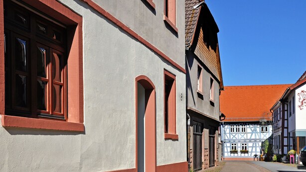 A narrow street lined with traditional half-timbered houses with red window frames and a clear blue sky.