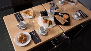 A breakfast table with croissants, a bowl of grapes, a bottle of water, and a newspaper. - Hostal La Parada (Getafe)