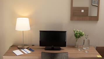 Habitación de hotel con un escritorio de madera, un monitor negro, una lámpara, una silla y un espejo en la pared.