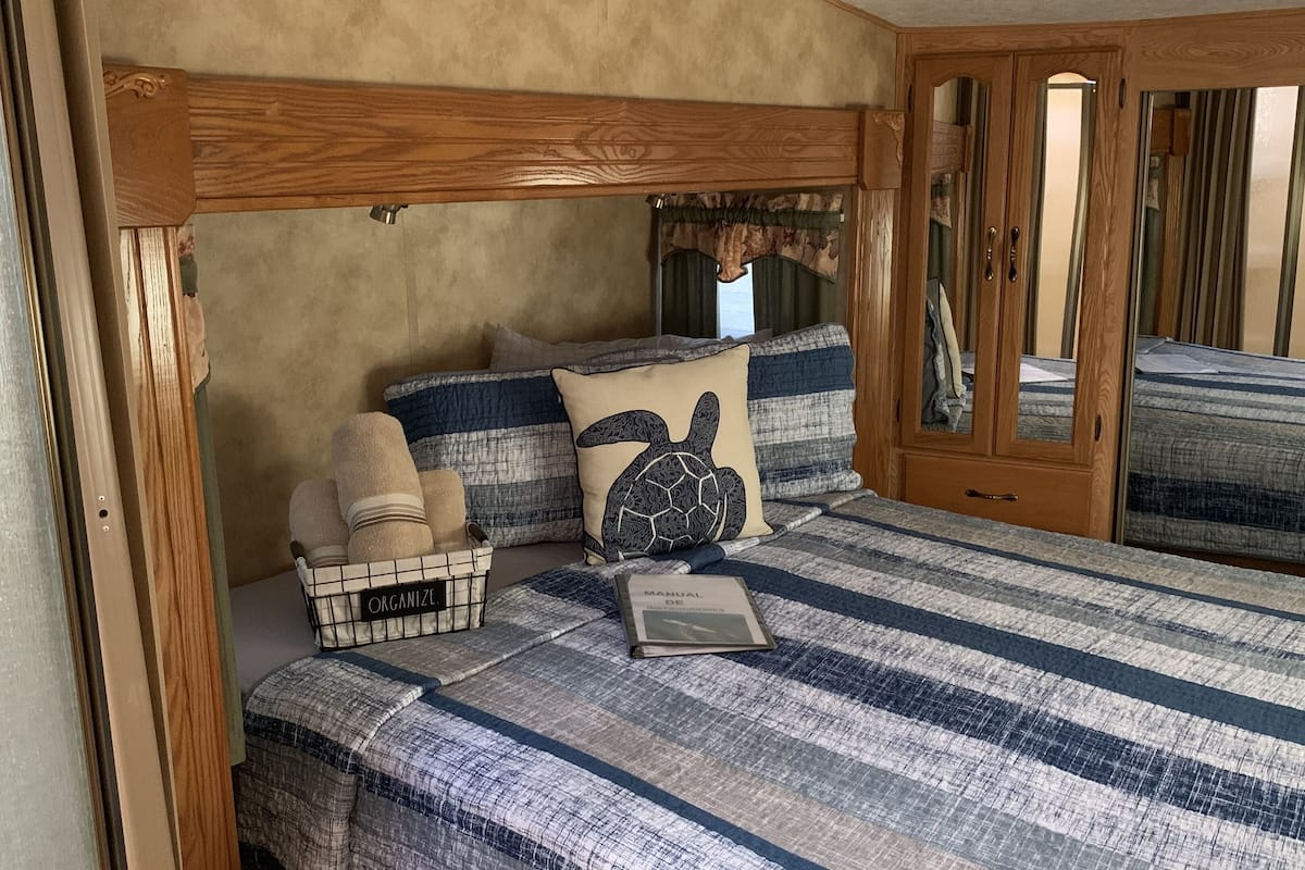 A bedroom with a wooden headboard, striped bedding, a basket labeled "ORGANIZE", and a book titled "MANUAL DE ORGANIZACION".