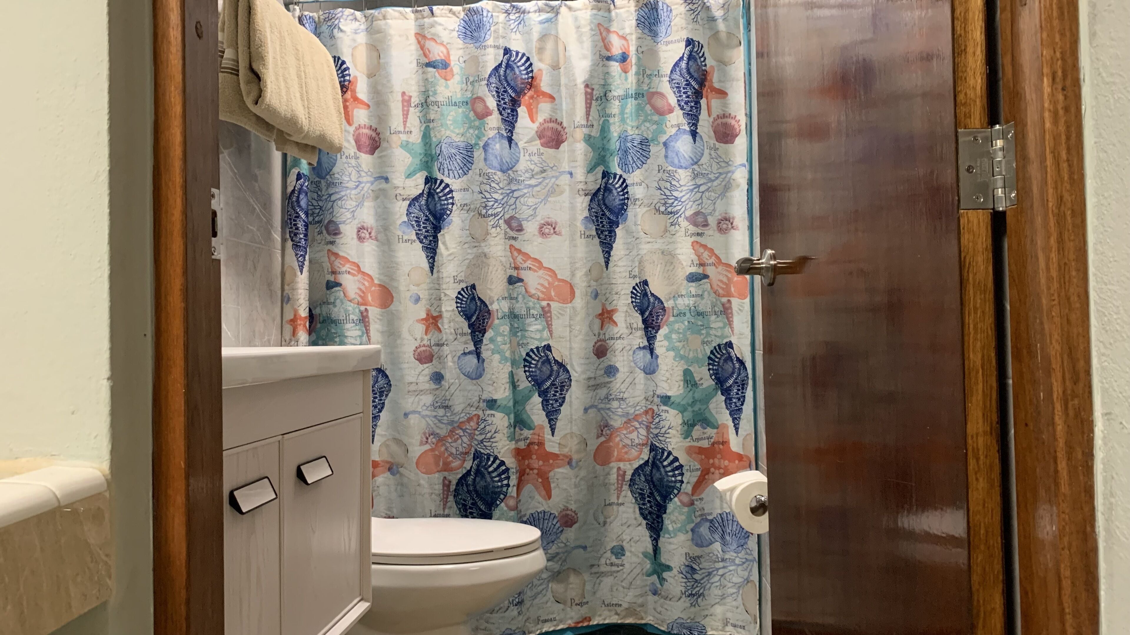 Ein Badezimmer mit Toilette, einer Holztür und einer Duschvorhang mit Meeresmotiven.