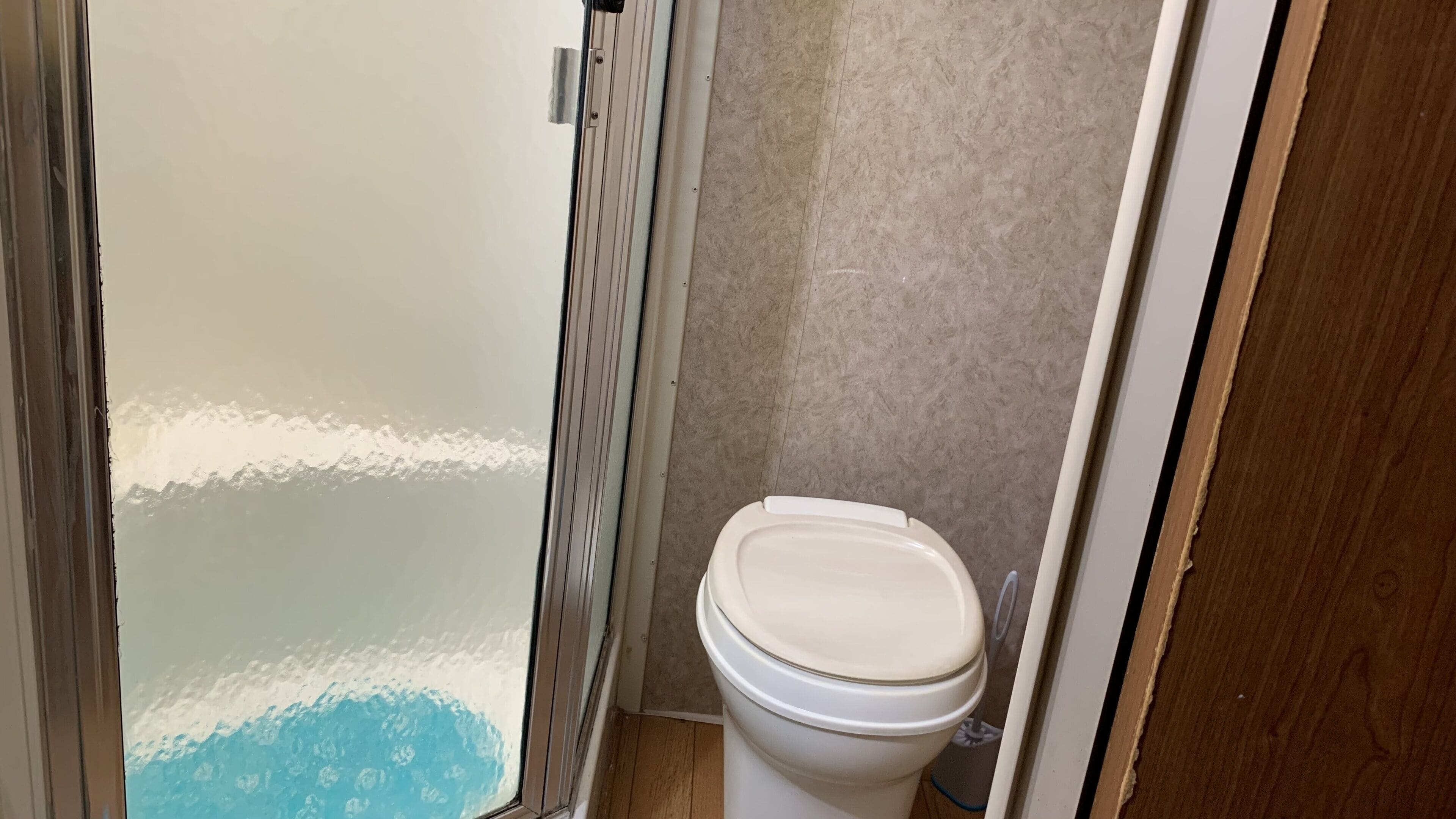 Une salle de bain comprenant des toilettes, un espace douche et un sol carrelé.