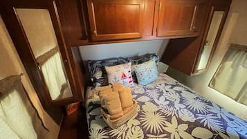 A compact bedroom with a bed, pillows, and a small stack of towels.