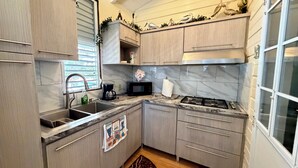 A compact kitchen with a sink, stove, microwave, and cabinets. - The Place at the Sea (Ponce)