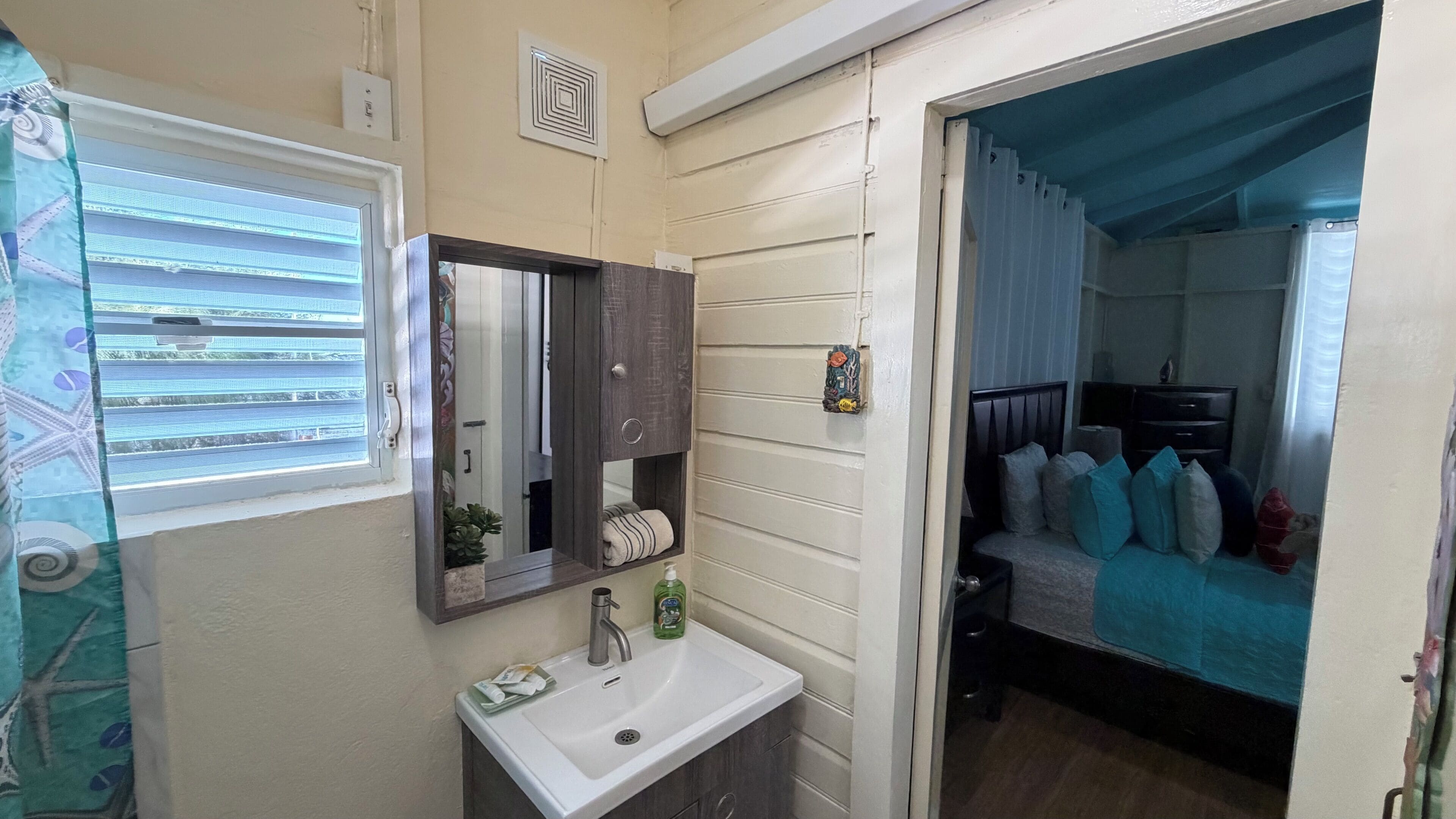 Une salle de bain avec une fenêtre, un lavabo, un miroir et une petite étagère contenant des articles de toilette.