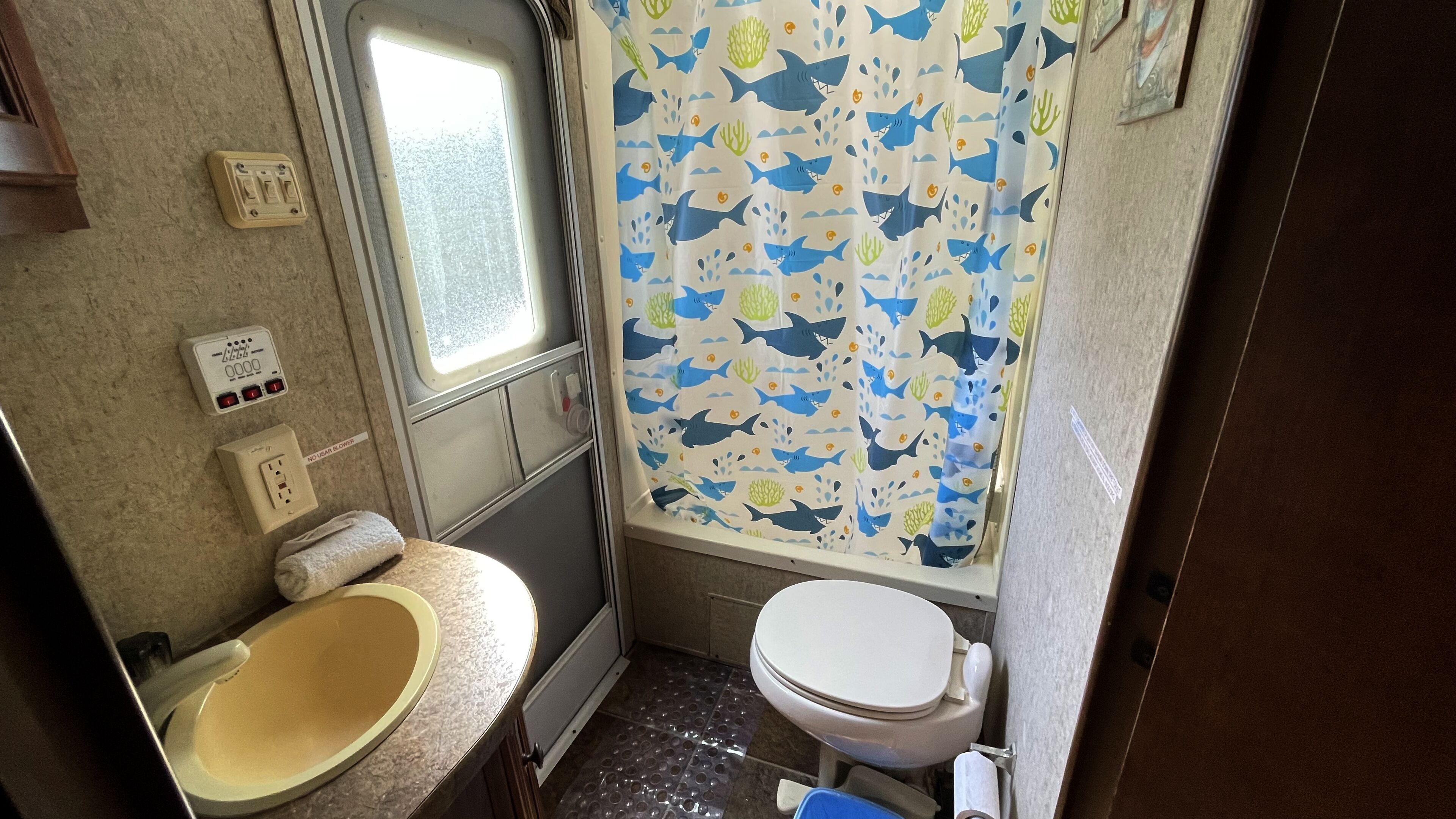 A small bathroom with a toilet, sink, and shower curtain with a shark and coral pattern.