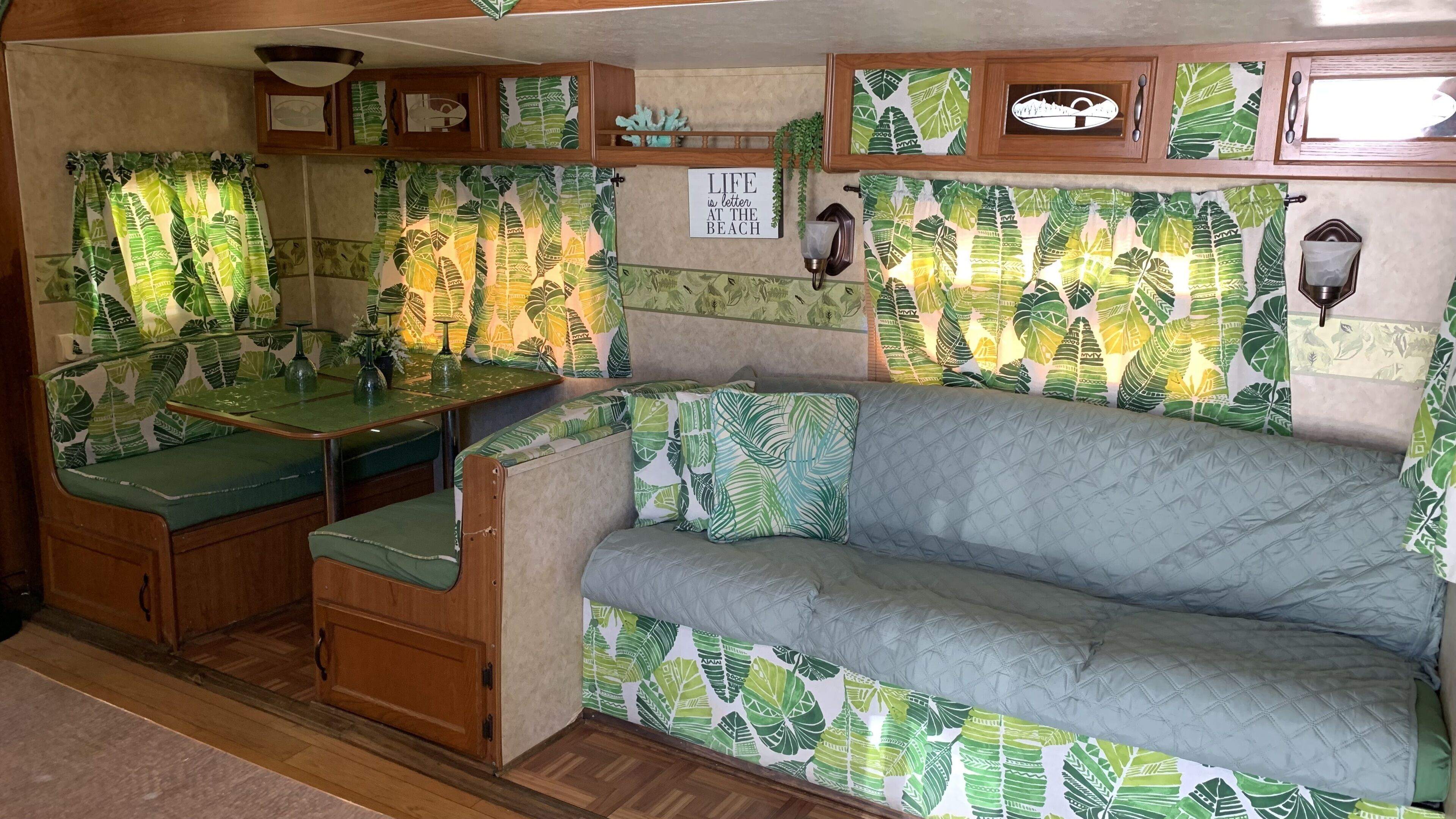 A compact RV interior with a kitchenette, a dining area, and a seating area with a couch and bench.