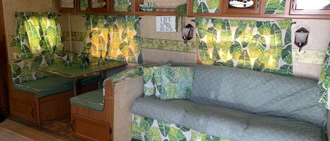 Interior compacto de autocaravana con kitchenette, comedor y zona de estar con sofá y banco.