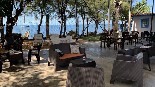 An outdoor seating area with wicker furniture, a table with a bottle, and a view of the sea. - The Place at the Sea (Ponce)