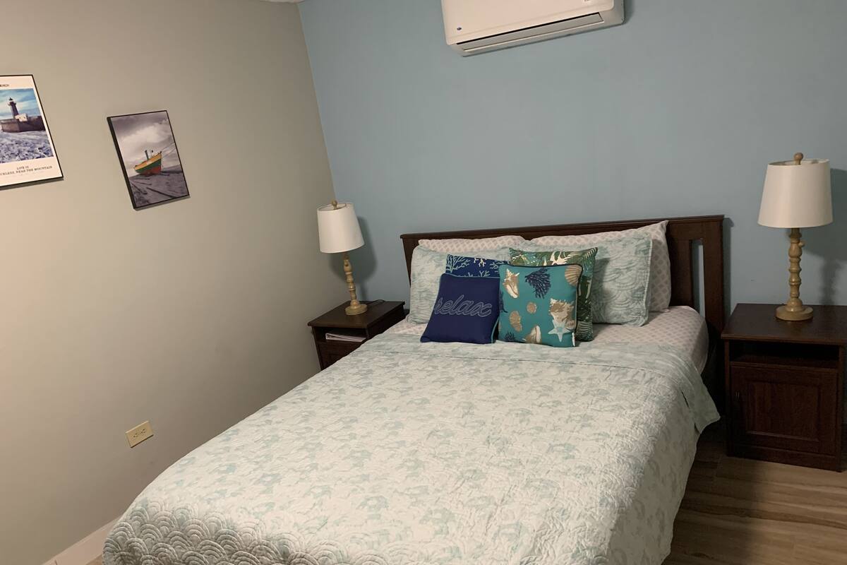 A bedroom with a bed, two nightstands, two wall-mounted lamps, and two framed pictures on the wall.