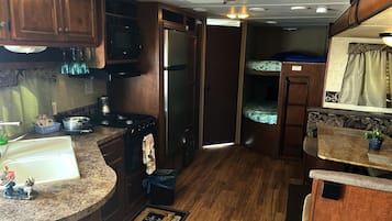 A compact RV kitchen with a stove, sink, microwave, and refrigerator.