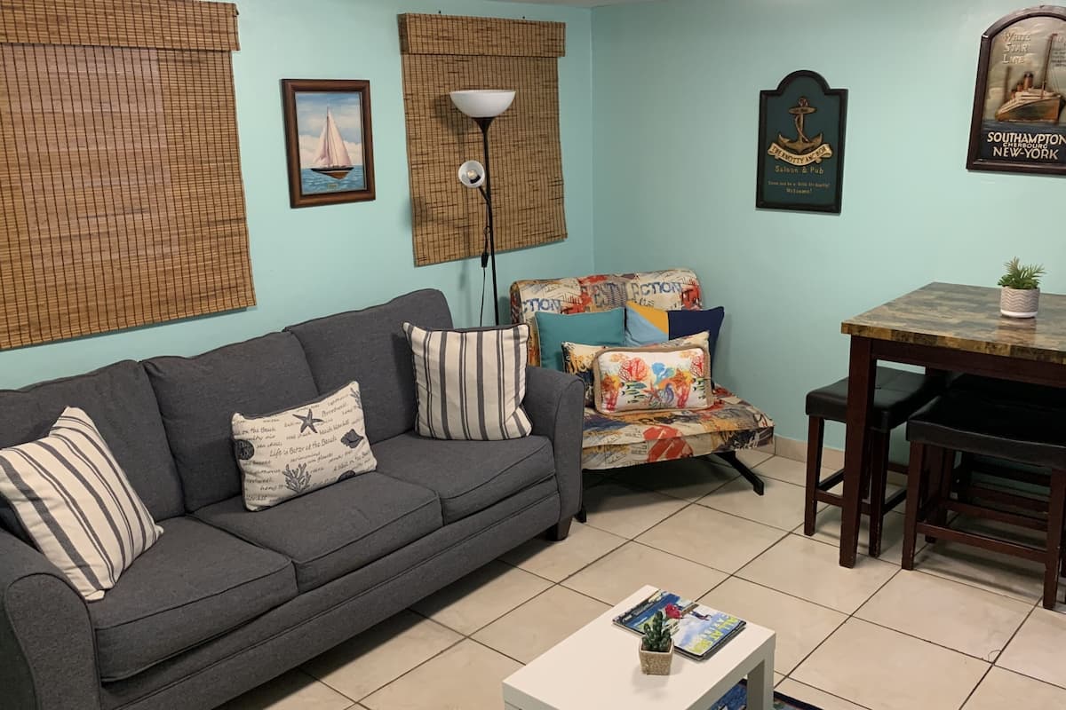 A living room with a grey sofa, a patterned armchair, a small table with a plant, and a poster on the wall.