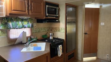 Una cocina compacta con armarios de madera, un microondas, un refrigerador de acero inoxidable, una estufa y un lavamanos con un jabonera.