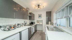 Een moderne keuken met witte aanrechtbladen, grijze kastjes, een inbouwoven en een raam met zonwering.