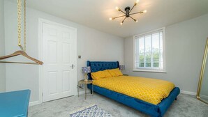 Een slaapkamer met een blauw bed, een hanglamp, een witte deur en een raam met jaloezieën.
