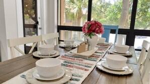 A dining table set with white plates, bowls, and glasses, with a vase of pink flowers and a box of condiments.