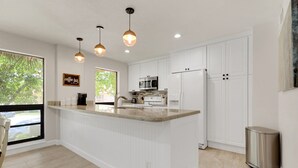 A modern kitchen with white cabinetry, a central island, pendant lighting, and a view of the outdoors.
