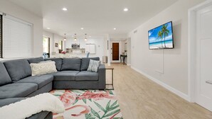 A modern living room with a grey sectional sofa, a floral area rug, and a kitchen in the background.