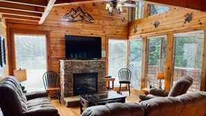 Un intérieur de chalet chaleureux avec une cheminée en pierre, des canapés en cuir et un téléviseur à écran plat.